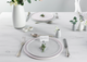 Elegant table setting with white plates, silverware, and floral arrangements on a light wooden surface.