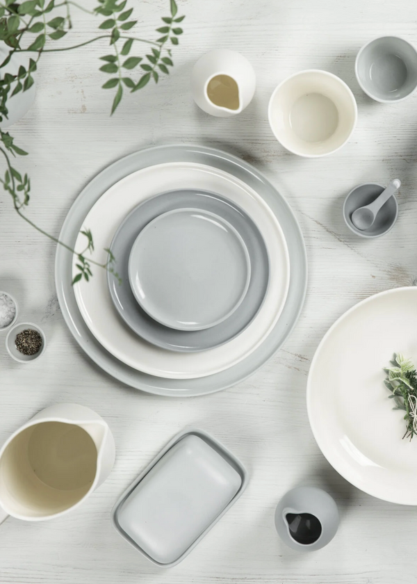 Collection of gray and white ceramic dishes on a light wooden surface with greenery.
