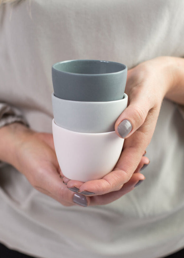 Two porcelain beakers in gray and pink colors, held in a person's hand, with a neutral background.