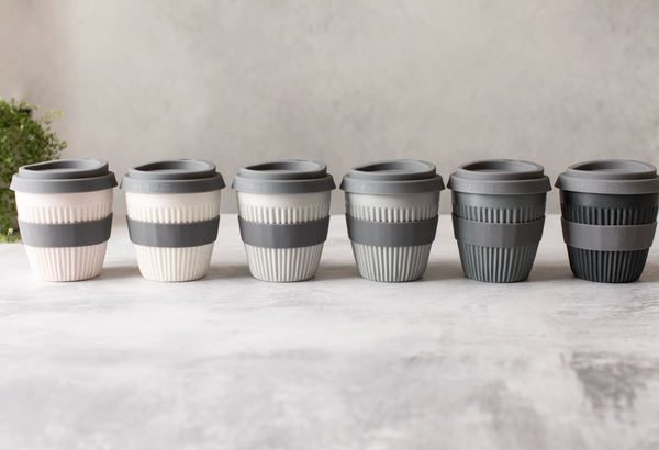 Set of six reusable coffee cups with gray lids on a light surface.