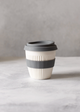Reusable coffee cup with a gray band on a marble surface with a plant in the background