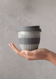 Hand holding a gray and white reusable coffee cup against a plain background