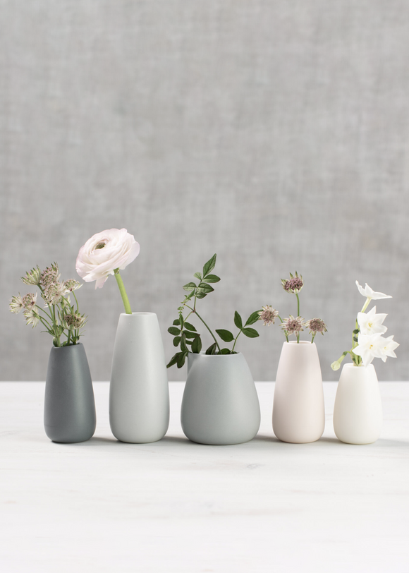 Set of five small vases with flowers on a white surface and gray background