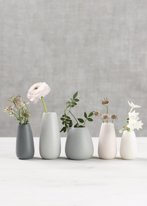 Set of five small vases with flowers on a white surface and gray background