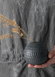 A person holding a round, textured, gray porcelain vase with a small bunch of dried flowers.