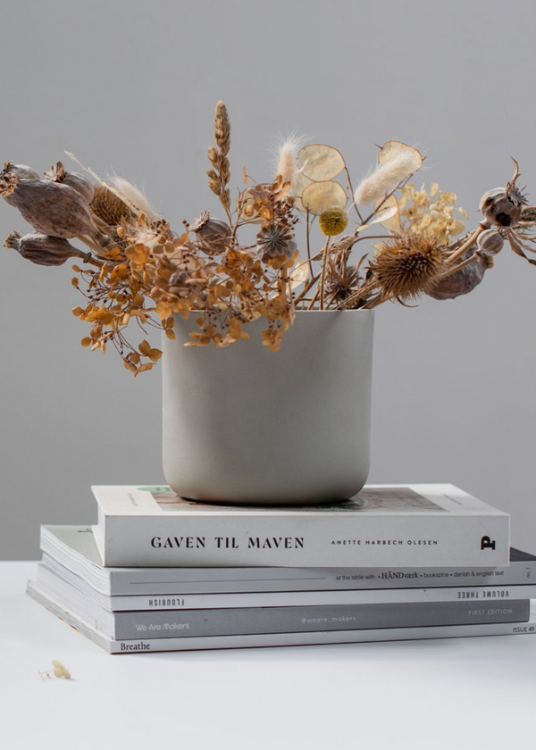 mid grey vase with dried flowers on a stack of books against a gray background