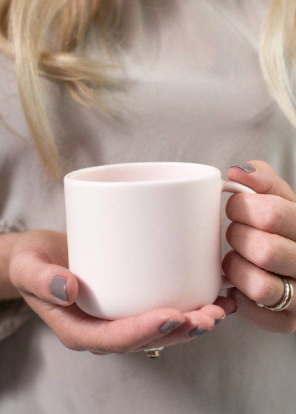 A person holding a white porcelain mug.