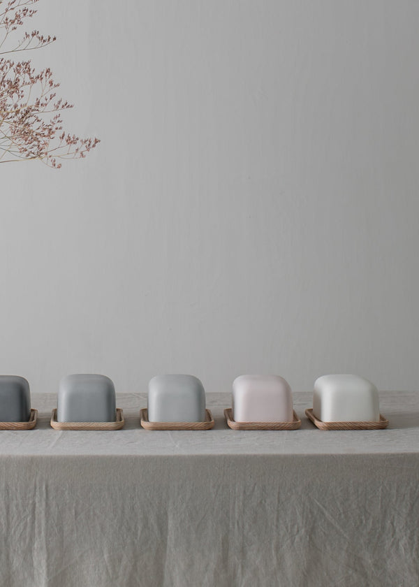 Row of small ceramic butter dishes on a light surface with a vase of dried branches in the background.