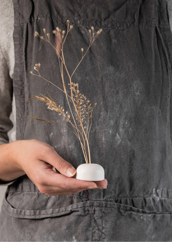 A person holding a small porcelain flower frog with three holes on the top, intended for inserting stems, such as dried flowers.