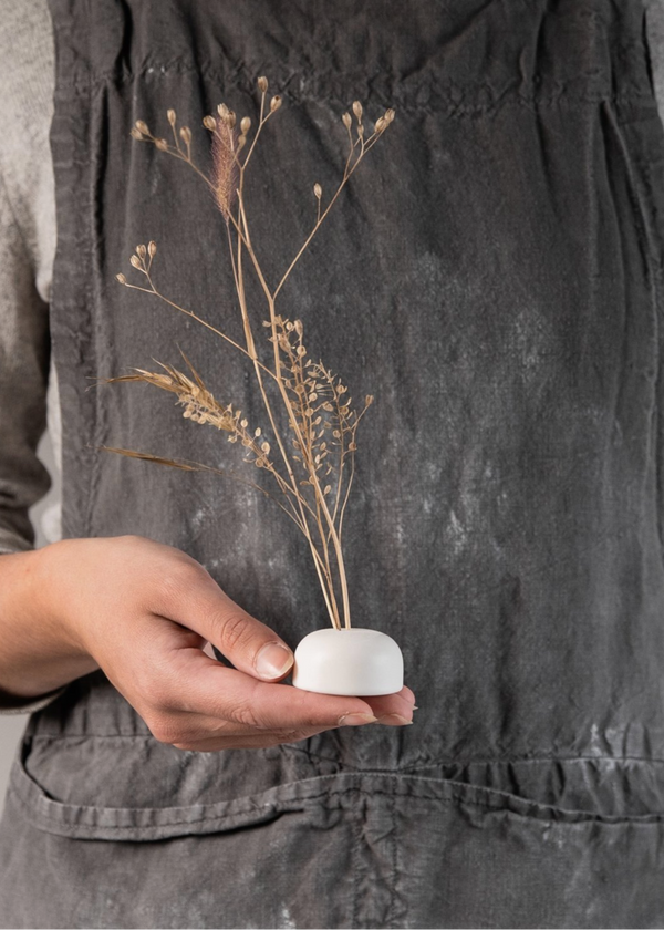 A person holding a small porcelain flower frog with three holes on the top, intended for inserting stems, such as dried flowers.