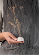 A person holding a small porcelain flower frog with three holes on the top, intended for inserting stems, such as dried flowers.