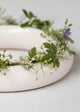 Pale pink ceramic ring vase with greenery and small flowers on a light gray background