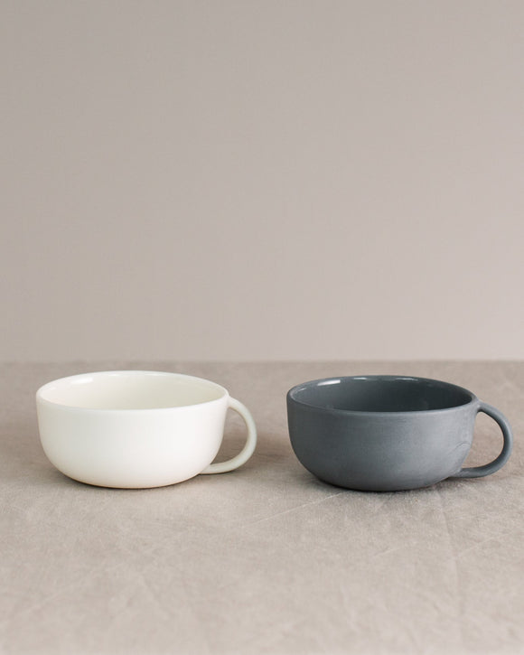 Two ceramic cups, one white and one gray, on a beige surface with a neutral background.