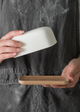 A person holding a white porcelain butter dish with a lid, with the wooden base separately shown below.