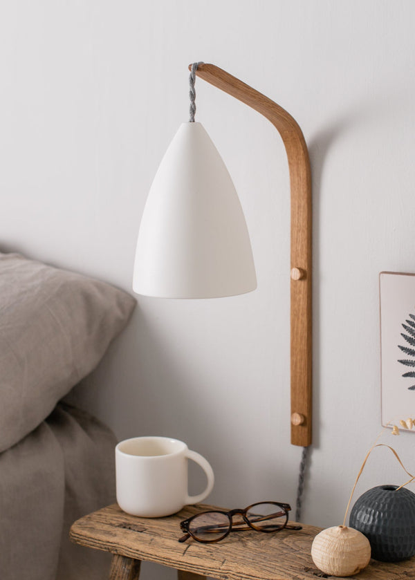 White mug next to a bed with a white wall and framed picture in the background.