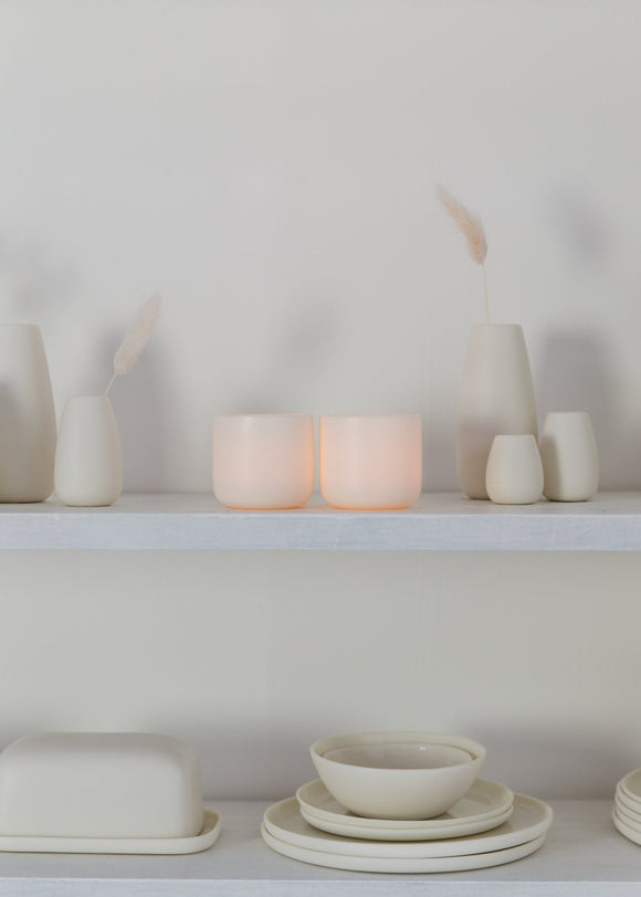 White porcelain candle and kitchenware on a white shelf against a white wall