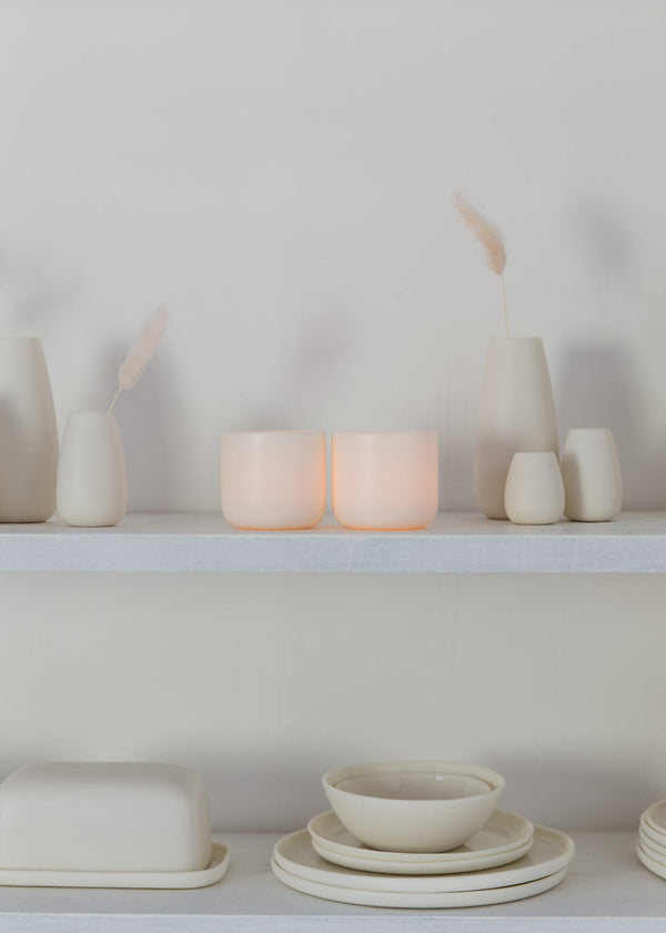 White porcelain candle and kitchenware on a white shelf against a white wall