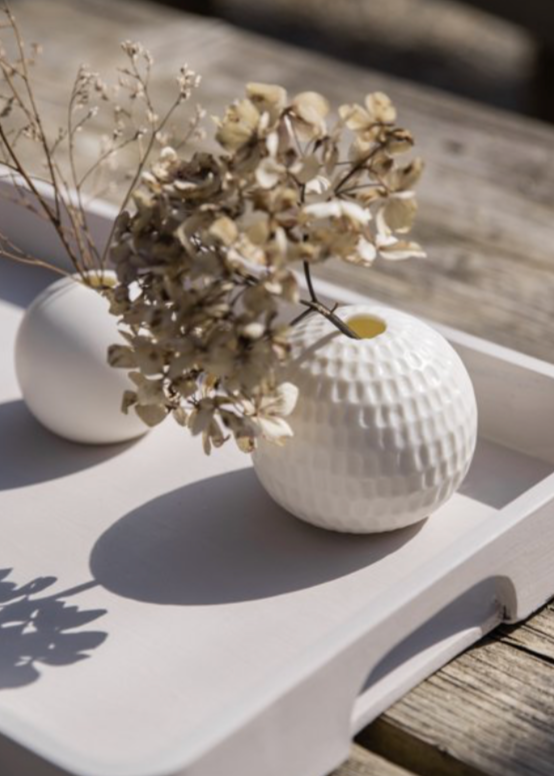 Two small white vases with dried flowers on a wooden surface
