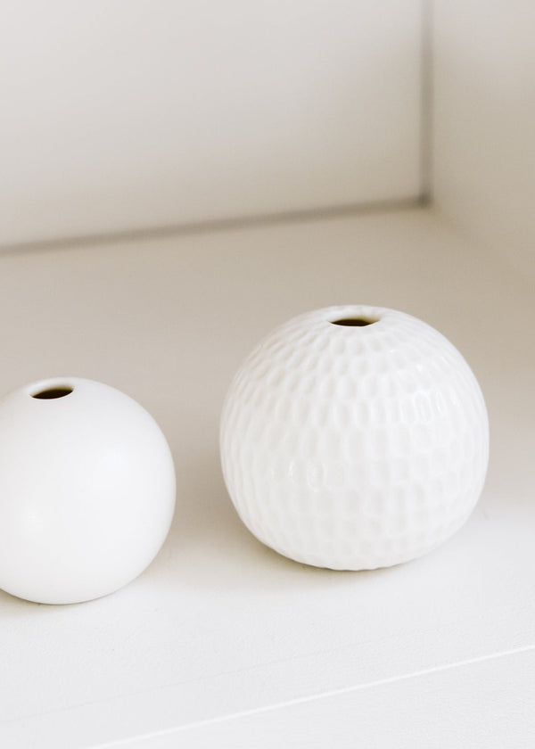 Two white spherical vases on a light surface with a neutral background