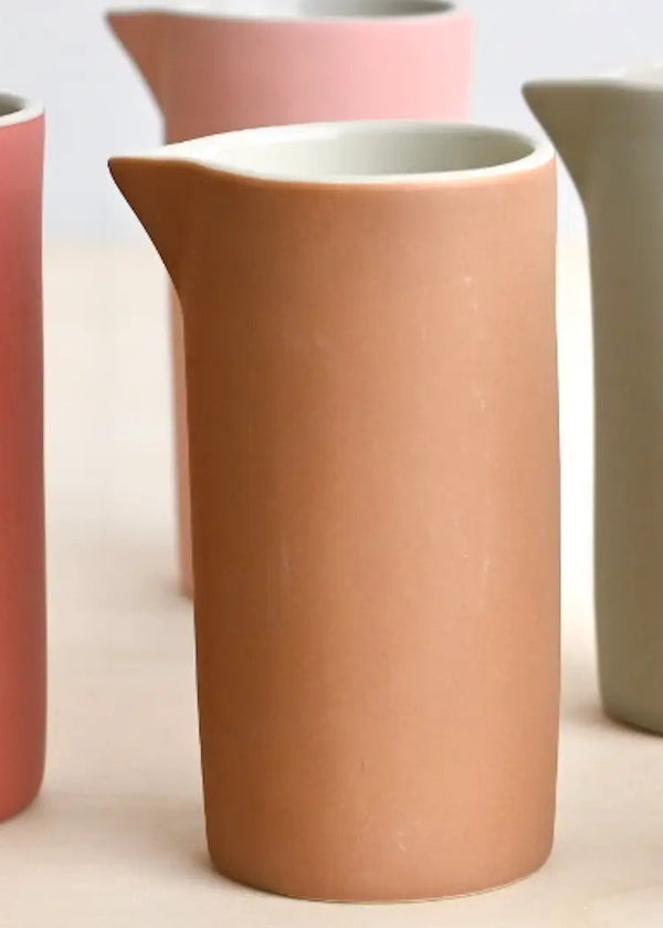 Set of ceramic mini milk jug in various colors on a light background