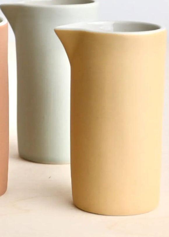 Three ceramic pitchers in pastel colors on a light background