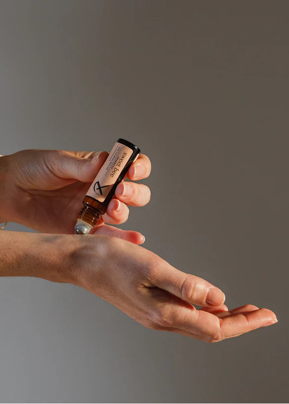 Person holding a small bottle of perfume with a gray background