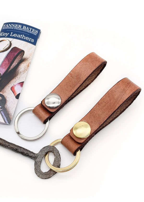 Brown leather key fob with gold and silver accents on a white background, featuring Fanner Bates packaging.