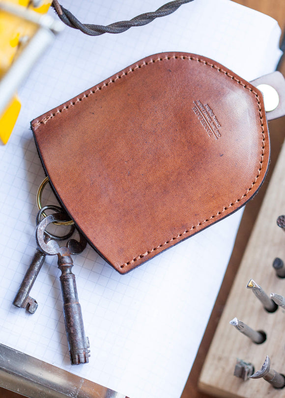 Brown leather keychain with keys on a white surface with tools in the background