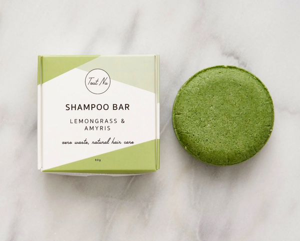 Green shampoo bar next to its packaging on a marble surface