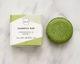 Green shampoo bar next to its packaging on a marble surface