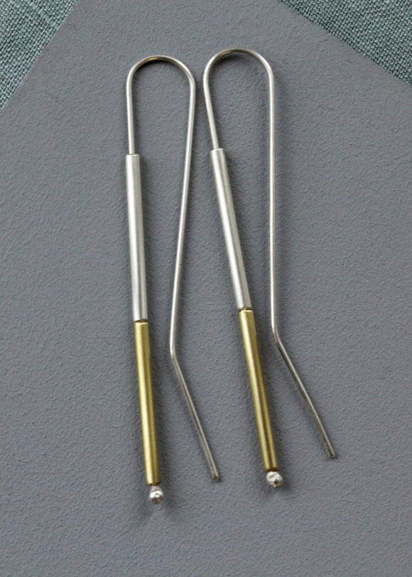 Two metal earings with gold accents on a gray surface