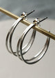 Silver hoop earrings on a gold stick against a gray background