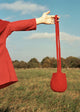 A red woolen bag being held up by a person against a grassy field backdrop.