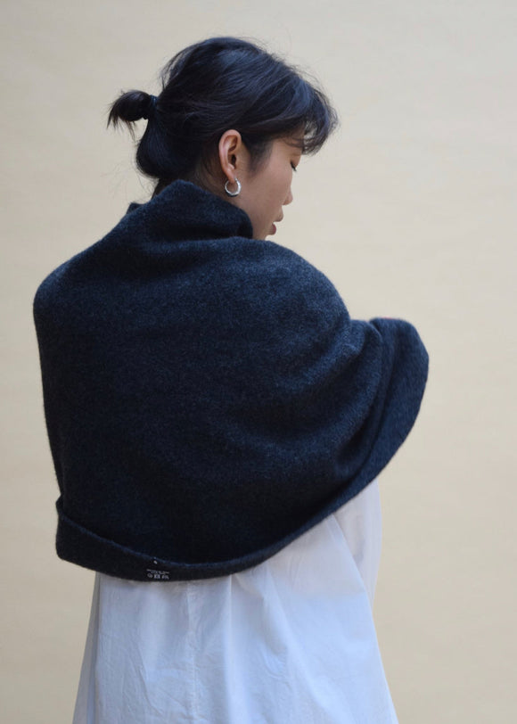 A person wearing a charcoal long poncho over a white dress, viewed from the back.