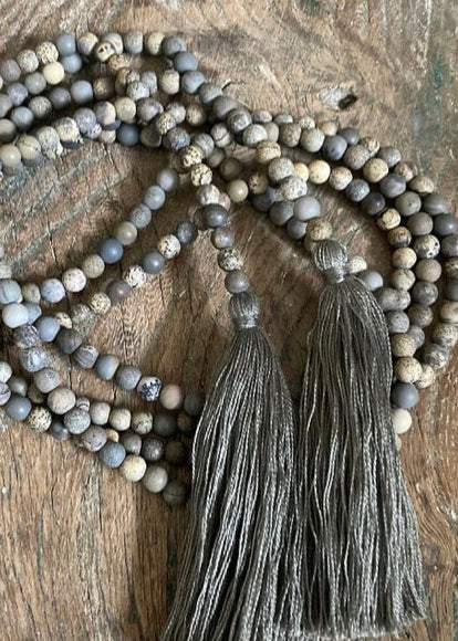 A beaded necklace with gray and brown tones, featuring various designs on the beads, laid out on a wooden surface.