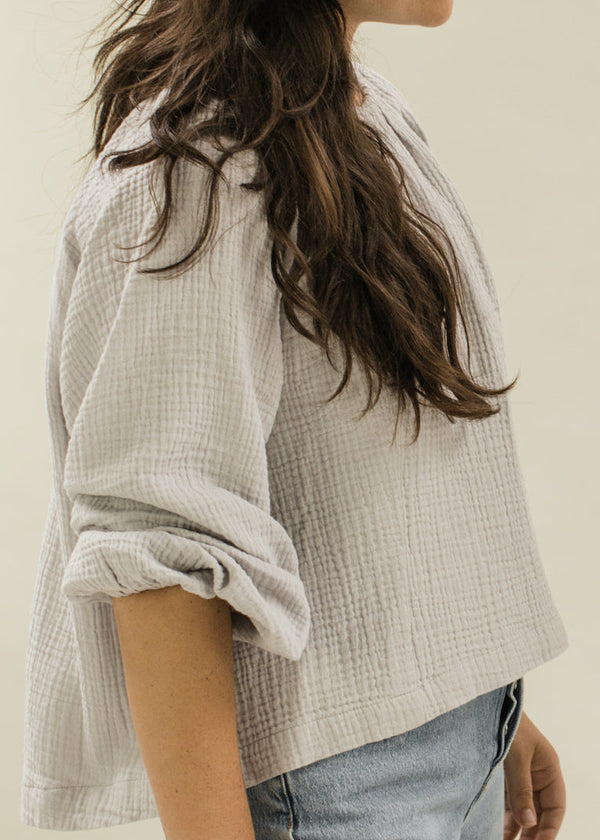 Person wearing a light gray checkered shirt with rolled-up sleeves against a neutral background