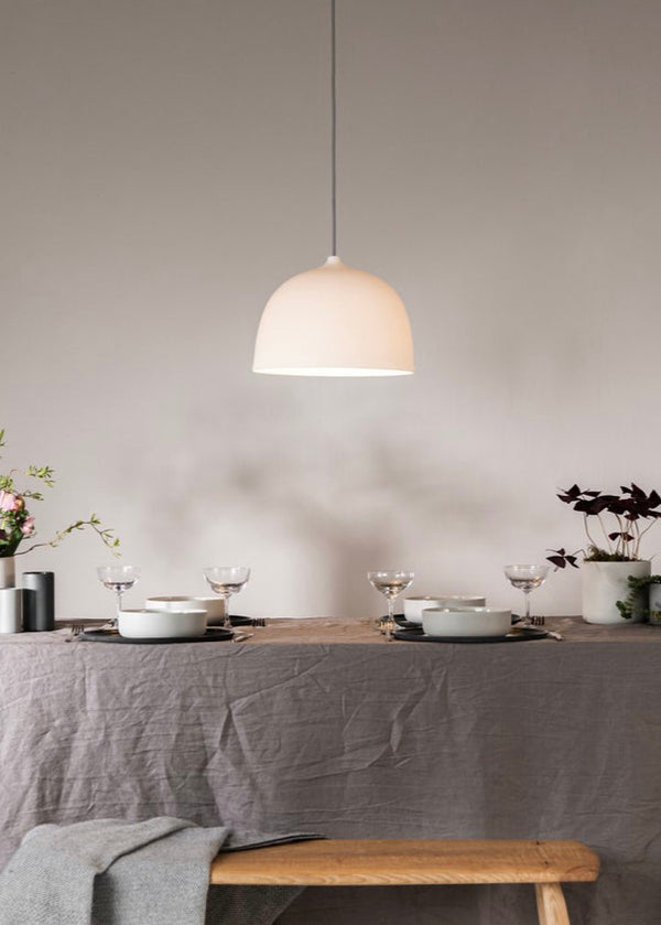A white porcelain pendant lamp hanging over a dining table set with dishes and flowers, in a room with light walls.