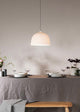 A white porcelain pendant lamp hanging over a dining table set with dishes and flowers, in a room with light walls.