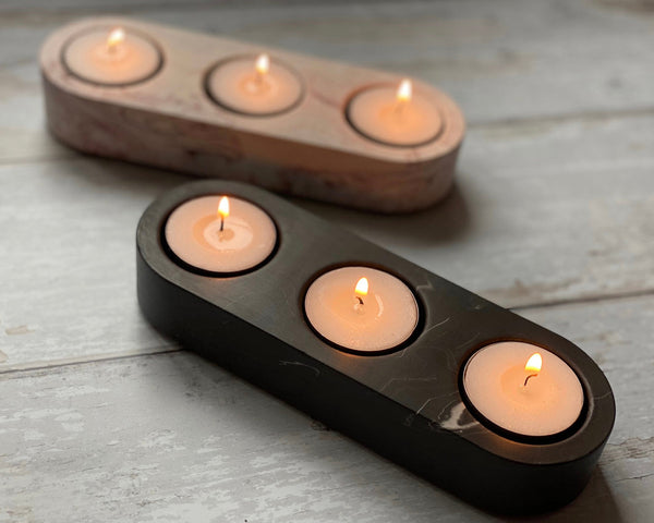 Two Jesmonite tealight holders with multiple lit candles placed within, on a wooden surface.