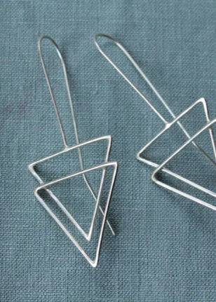 A pair of geometric triangle silver earrings displayed on a grey textured surface.
