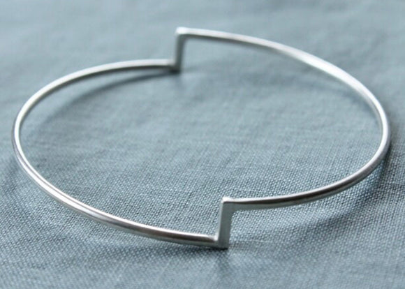 A single silver stepped bangle bracelet displayed on a textured blue surface.