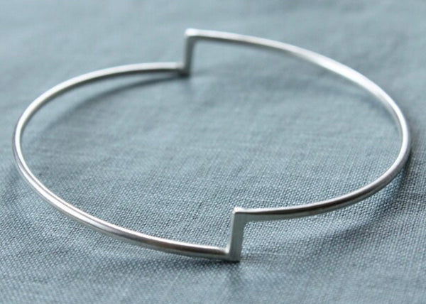 A single silver stepped bangle bracelet displayed on a textured blue surface.