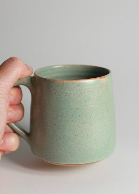 A hand holding a green stoneware mug.