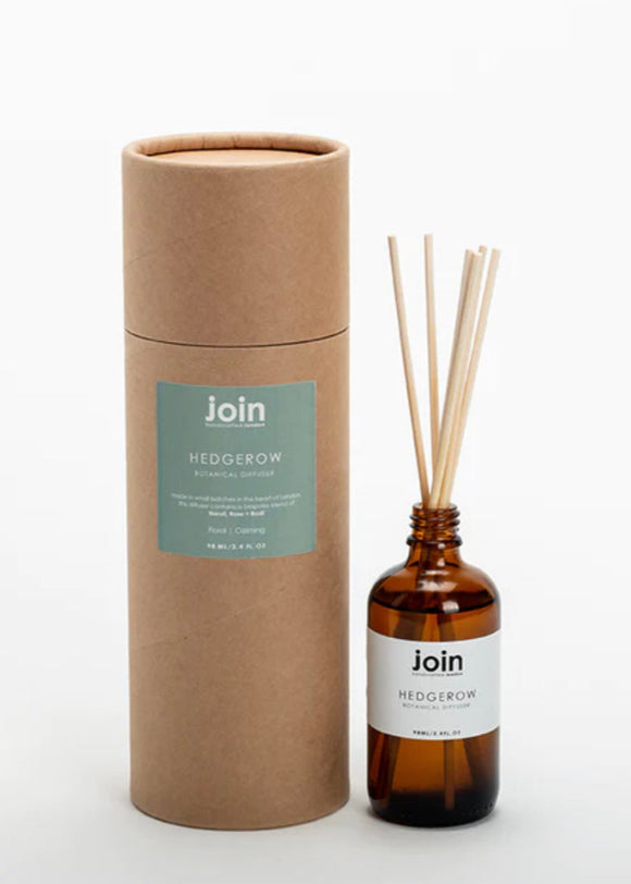A luxury botanical room diffuser by Join, featuring a brown cylindrical packaging and a amber glass bottle with diffuser sticks inside. The label on the bottle reads 'Hedgerow'.