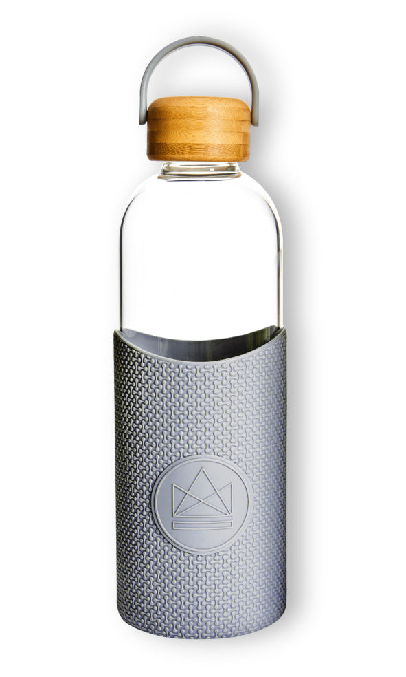 A clear glass water bottle with a silver geometric patterned sleeve and a bamboo lid.