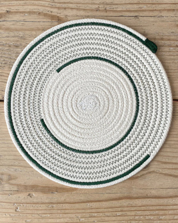 A round placemat with a white and green geometric pattern, placed on a wooden surface.