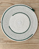 A round placemat with a white and green geometric pattern, placed on a wooden surface.