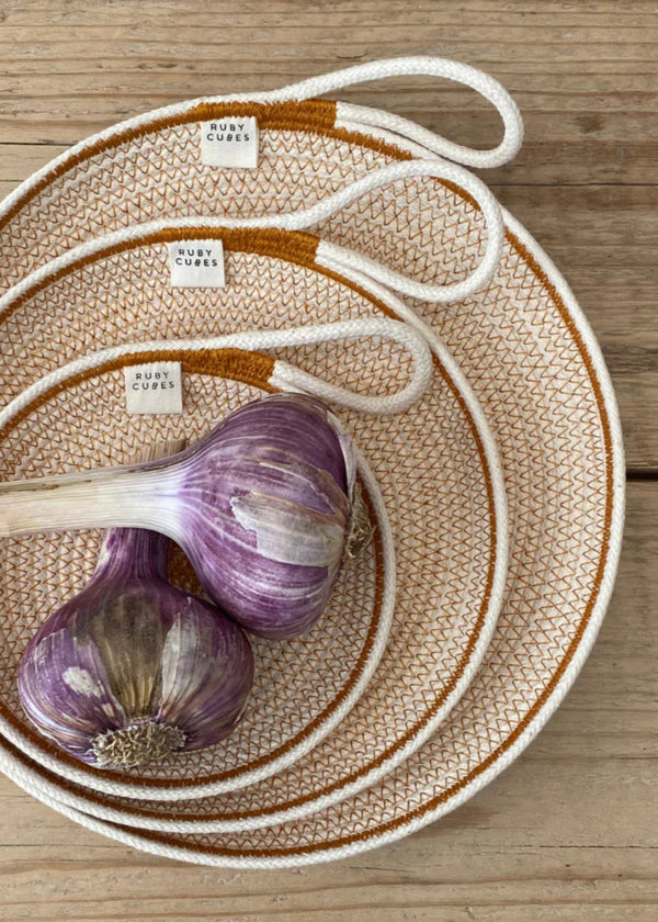 A set of three rope plates in varying sizes with a garlic bulb and two cloves on the largest plate, displayed on a wooden surface.