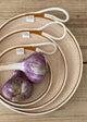 A set of three rope plates in varying sizes with a garlic bulb and two cloves on the largest plate, displayed on a wooden surface.